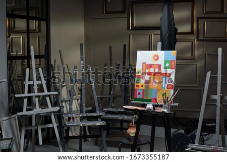 Interior of classroom in contemporary art studio with group of easels and picture on one of them with painting stuff