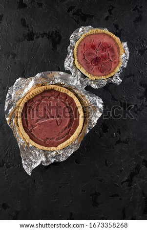 Kitchen failure concept. Cracked strawberry pies in foil on black background top view copy space
