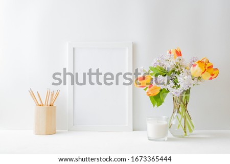 Home interior with decor elements. Mockup with a white frame yellow tulips and branches of lilac in a vase on a light background