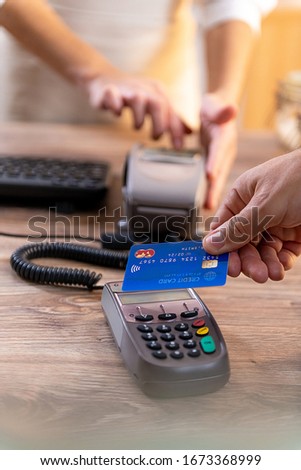 Closeup of Caucasian right hand, holding a blue credit card and paying at the POS terminal Royalty-Free Stock Photo #1673368999