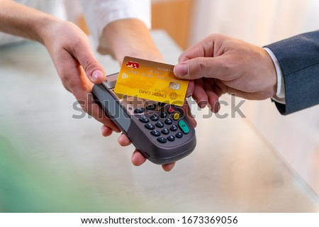 Closeup of Caucasian right hand, holding gold credit card on a PIN PAD held by a woman's hands Royalty-Free Stock Photo #1673369056