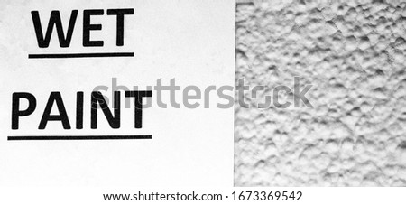 A black and white/monochrome sign with the words Wet Paint against a rough textured wall with room for further text/copy space.  