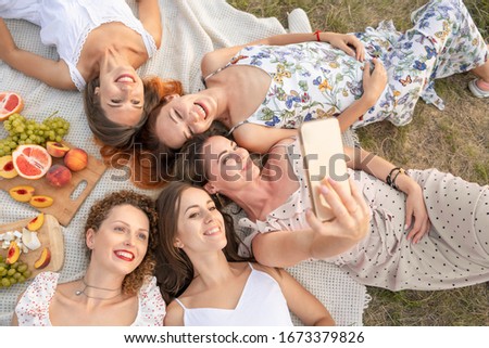 View from above. The company of beautiful girlfriends have fun and enjoy a picnic outdoors and take pictures on a mobile phone.