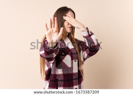 Young caucasian woman isolated on beige background making stop gesture and covering face