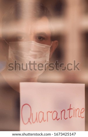 A portrait of man indoor behind the window holding paper with word Quarantine. People, medicine and healthcare concept. Coronavirus epidemic