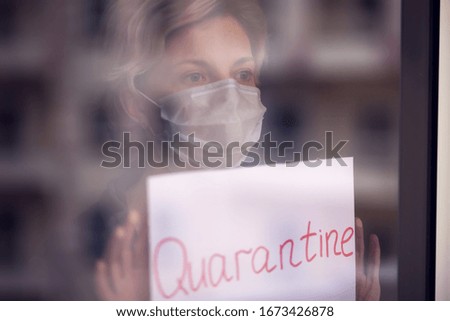 A portrait of woman indoor behind the window holding paper with word Quarantine. People, medicine and healthcare concept. Coronavirus epidemic