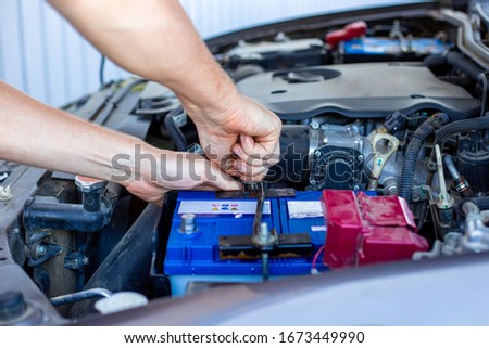 repair and installation of the battery under the hood of a car, a man works in a car service Royalty-Free Stock Photo #1673449990