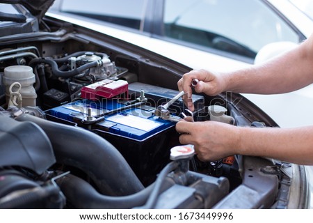 a man tightens with a wrench bolts for fastening a new battery, installing spare parts for a car Royalty-Free Stock Photo #1673449996