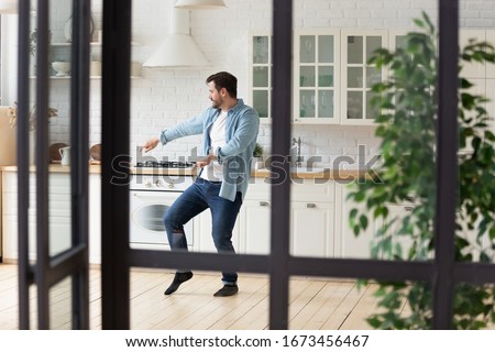 Funny positive man dancing in modern kitchen alone, moving to favorite popular music, celebrating relocation or weekend, happy handsome guy having fun at home, enjoying leisure time Royalty-Free Stock Photo #1673456467