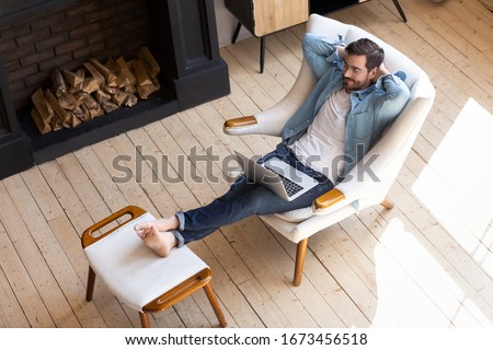 Peaceful young man resting with closed eyes in cozy armchair with laptop top view, successful serene male sitting with hands behind head, enjoying lazy leisure time, daydreaming during break at home Royalty-Free Stock Photo #1673456518