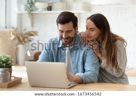 Happy young man and woman hugging, using laptop together, looking at screen, loving couple shopping or chatting online, using internet banking services, reading news in social network Royalty-Free Stock Photo #1673456542