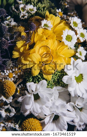Wedding rings and engagement ring lie on a beautiful bouquet of wildflowers. Beautiful bouquet of daisies with rings of the bride and groom.