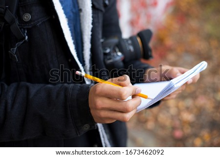 Professional photographer making notes preparing for photoshoot. Young photographer shooting autumn landscapes, choosing the best time to shoot, writing some setting to his notebook