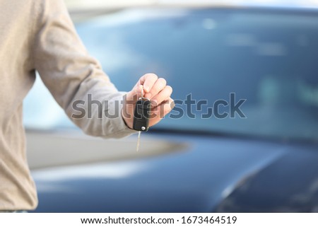Man holding key in modern auto dealership, closeup. Buying new car