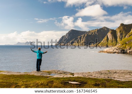 Amazed tourist enjoying views on the coast of fjord with stunning mountains on Lofoten islands in Norway