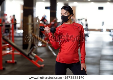 Coronavirus covid-19 prevention, fitness girl with a medical mask holding a dumbbell . Fighting viruses. Royalty-Free Stock Photo #1673535190