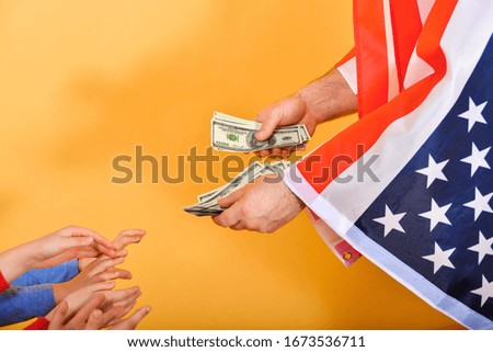 The hand of a man flying the American flag hands money to children’s hands, the concept of dependence on the USA.
