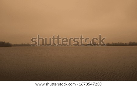 A wide landscape of a dark gray lake and forest. Overcast sky