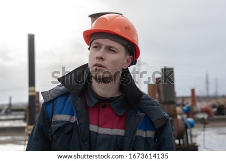 Worker builder on the roof of the factory. dressed in a dirty working uniform. on the head is an orange construction safety helmet. serious look into the distance. working days
 Royalty-Free Stock Photo #1673614135