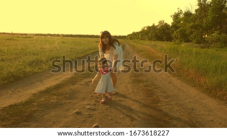Mother and baby rest in park. concept of a happy childhood. little daughter and mom walk along road past field. child plays running away from mom. happy family with child walks in countryside.
