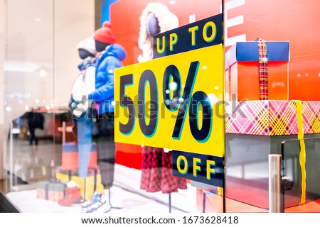Up to 50% off price reduction promotion sign on window display at clothes clothing store or apparel winter shop in Europe with mannequins