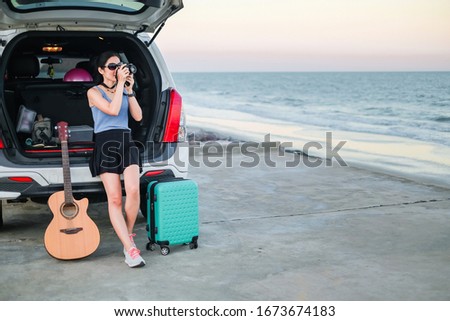 woman traveler have camera and guitar sitting on hatchback of car and looking for view of the sea and sunset  on vacation.travel concept.
