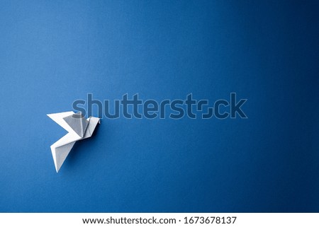 Origami pigeon on a blue isolated background. World Peace Day concept. Close up studio photo.