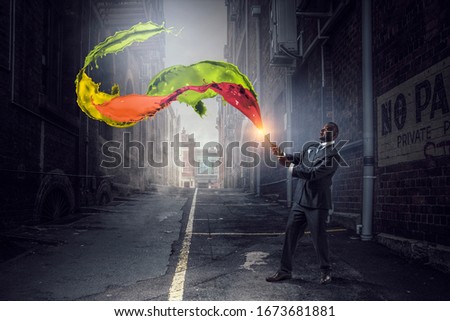 Conceptual image of ambitious and creative businessman in black suit holding paintbrush in hand