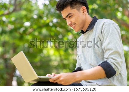Asian student Using laptop in college. Person side view of Happy man typing on notebook with green background. Technology Concept.