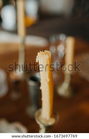 Vertical photo of an old yellow leaking candle against a blurry vintage-style table.