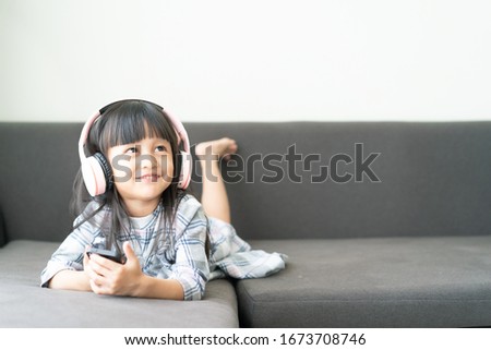 Adorable 4 years old asian little girl is lying and watching cartoon in smartphone on the sofa with happy moment, concept of kid in modern lifestyle and how parent advice child to using the technology