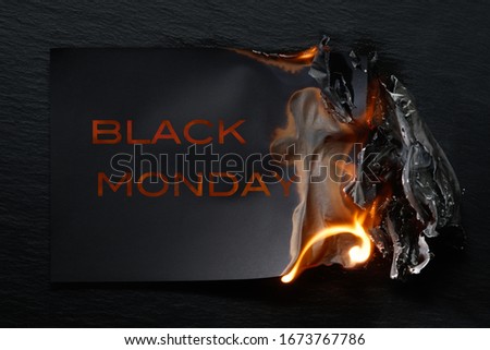 Burning piece of black paper with the word "BLACK MONDAY"on a black background.