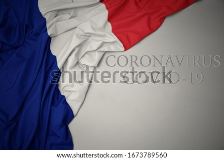 waving colorful national flag of france with text coronavirus covid-19 on a gray background.