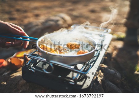 person cooking fried eggs in nature camping outdoor, cooker prepare scrambled omelette breakfast picnic on metal stove, tourist on recreation outside; campsite lifestyle Royalty-Free Stock Photo #1673792197