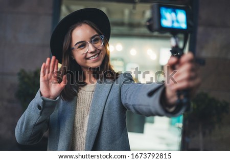 Female vlogger recording with digital camera. Smiling young woman taking selfie video on light night city. Traveler blogger shooting video for shoot social media