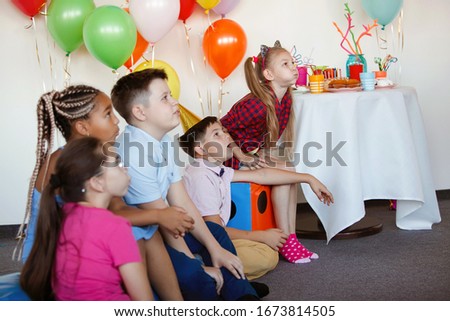 Bright, cute children celebrate a birthday. Multinational party, balloons, caps, smiles and joy, adolescents carefully watch the performance.