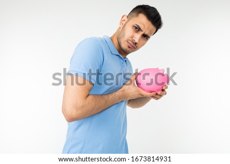 man looks suspiciously holding a piggy bank in his hands on a white studio background
