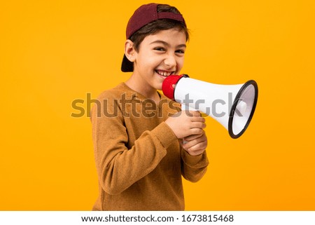 attractive european boy shouts in a megaphone in his hands for a poster on an orange studio background