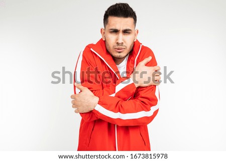 man in a sports red suit shrinks from the cold hugging himself on a white background with copy space