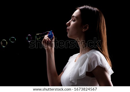 A beautiful slender girl in a white dress lets soap bubbles on a black background, adults are engaged in children's entertainment