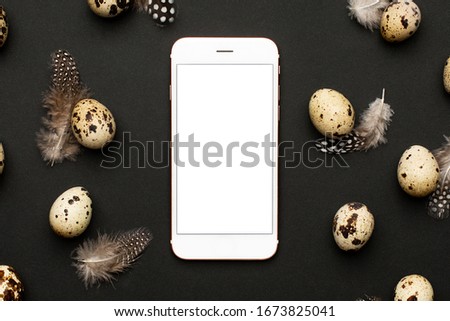 Mobile phone and quail eggs with feathers on a black background. Holiday easter, minimalistic black composition