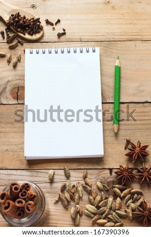 Notebook with green pencil and aromatic spices on wooden table