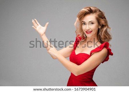 Handsome lady shows her hands and smiles, picture isolated on grey background
