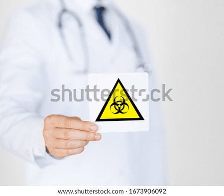 health, medicine and pandemic concept - male doctor holding boihazard caution sign