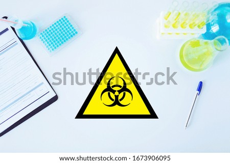 science, medicine and pandemic concept - biohazard caution sign in scientific laboratory table with test tubes and vaccine samples