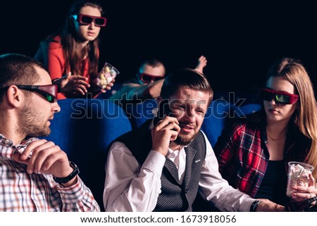 The guy speaks on the phone and interferes with watching a movie in a movie theater. Stock photo of a group of people in the cinema.