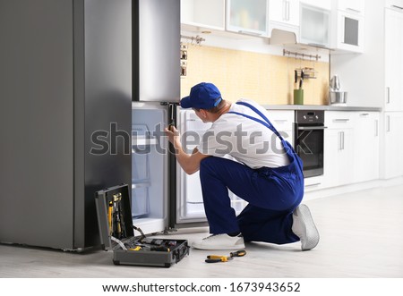 Male technician with screwdriver repairing refrigerator in kitchen Royalty-Free Stock Photo #1673943652