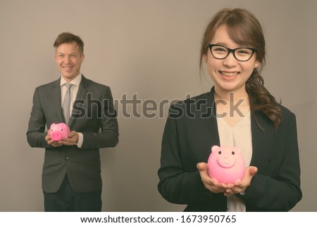 Young businessman and young Asian businesswoman against gray background