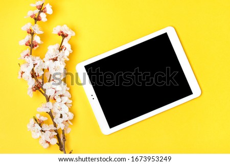 Bouquet of sprigs of apricot tree with flowers, white tablet on yellow background. Place for text. The concept of spring came, mother's day, 8 march. Top view. Flat lay Hello march, april, may Mock up