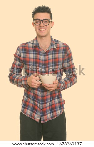 Studio shot of happy young man smiling while holding coffee cup
